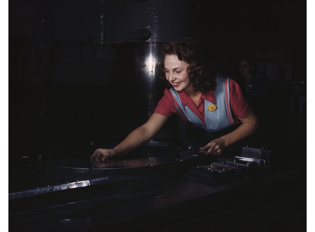 A worker places metal parts on Masonite before they slide under the multi-ton hydropress at the North American Aviation plant