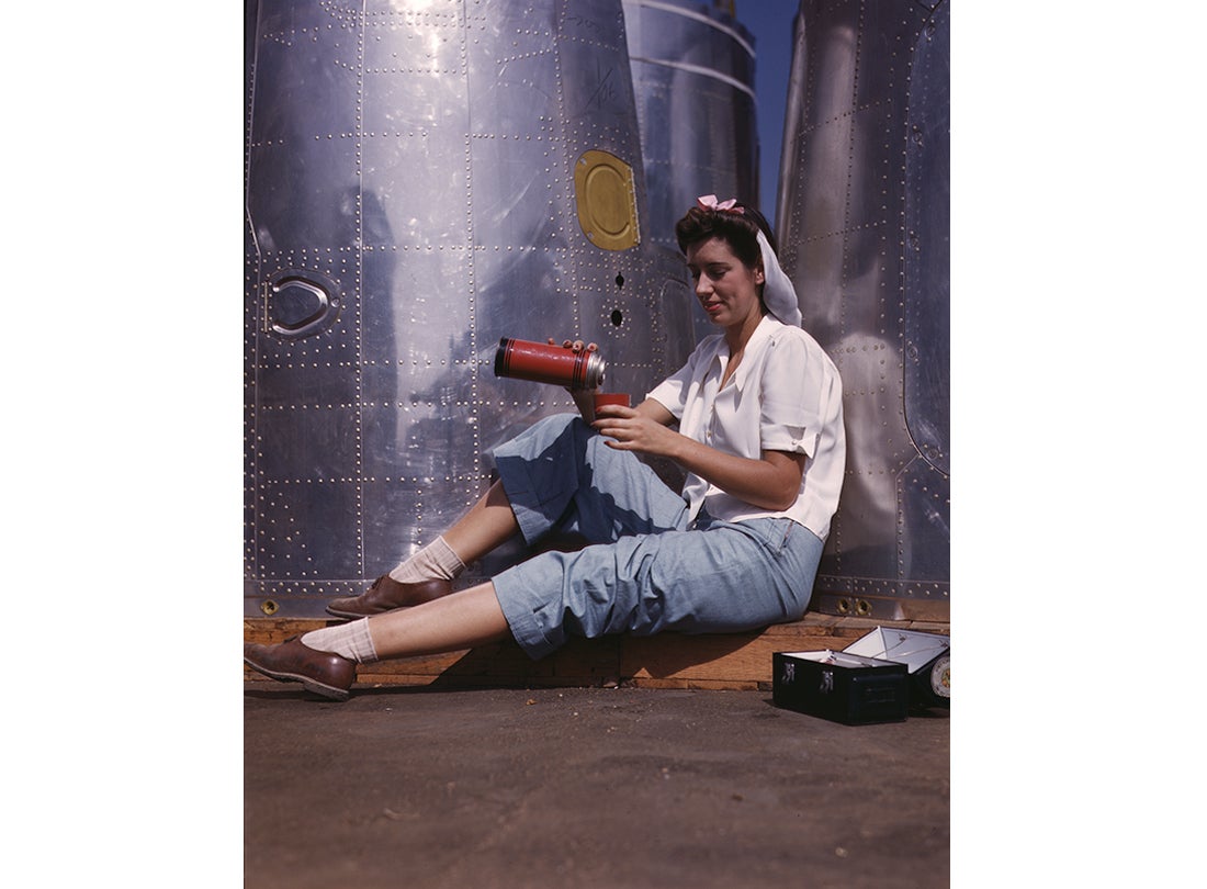A worker during her lunch break with heavy bomber nacelle parts in the background at the Douglas Aircraft Company plant