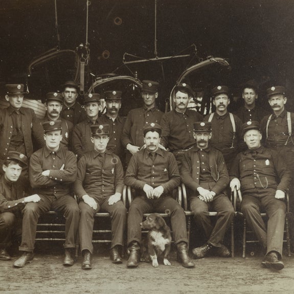 Firemen with dog and engine in background  late nineteenth century