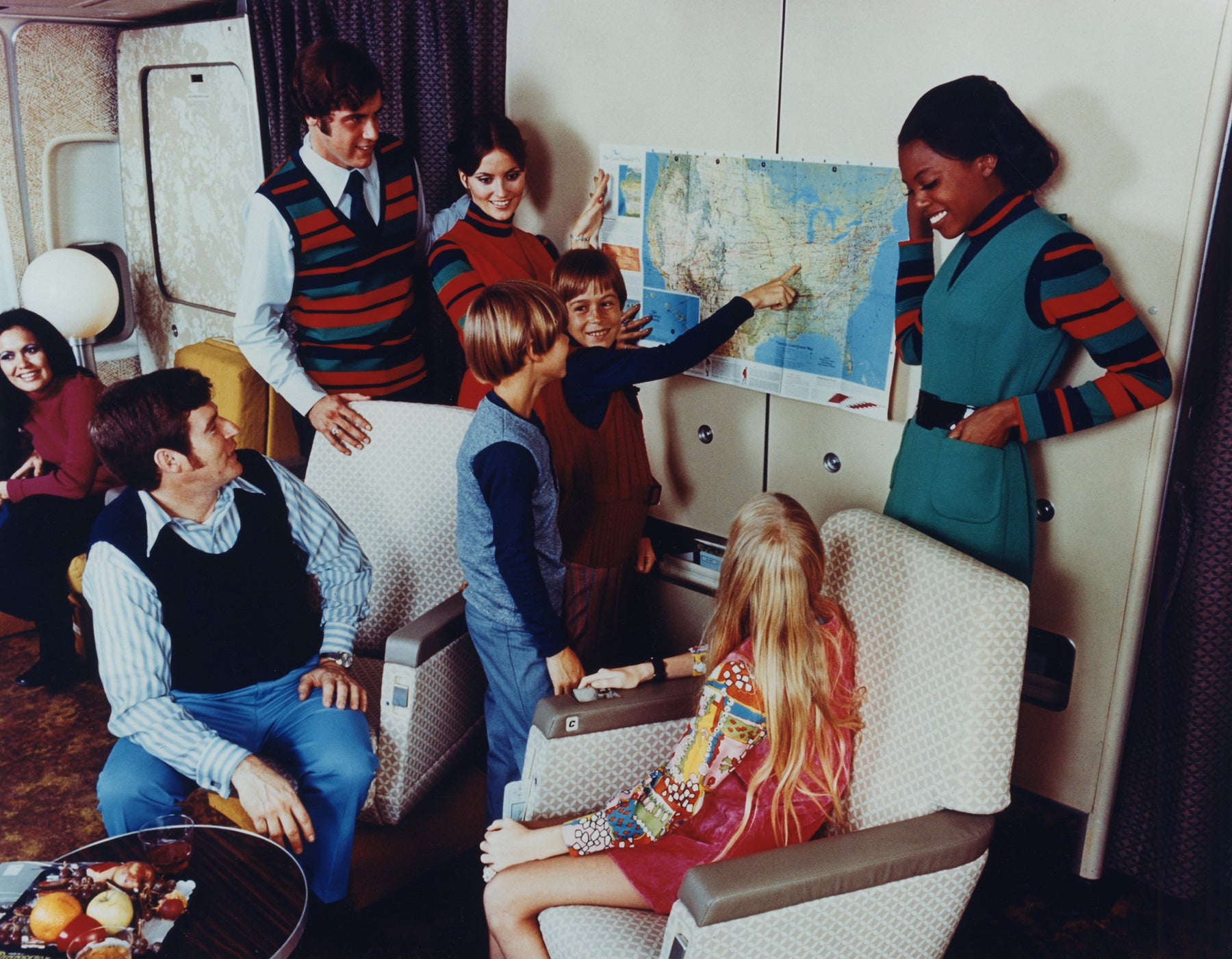 United Air Lines flight attendants review route map with a family aboard a Boeing 747 widebody airliner  c. 1973