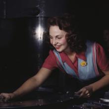 A worker places metal parts on Masonite before they slide under the multi-ton hydropress at the North American Aviation plant