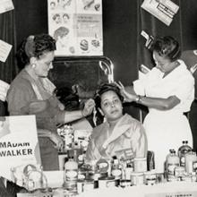 Hair demonstration in the Madam C. J. Walker booth at the Regional Beauty College Convention; Walker’s attorney F. B. Ransom, who played a significant role in her business and personal life, is pictured on the left