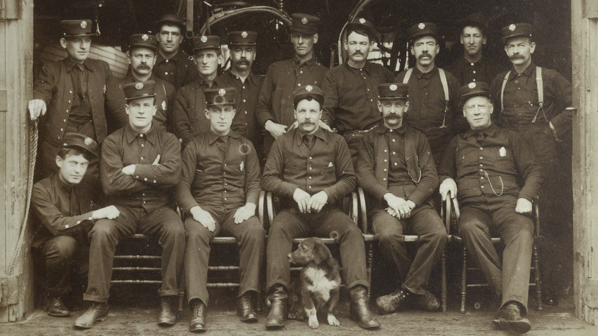 Firemen with dog and engine in background  late nineteenth century